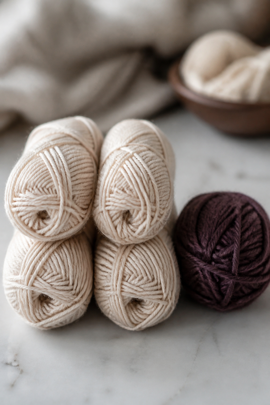 Four balls of smooth pale plied worsted yarn next to a dark single ply yarn, shown for comparison.
